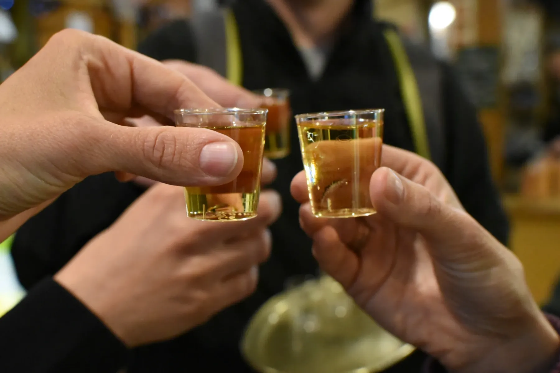 Close-up of three hands toasting with small tasting glasses of amber liquid in Krakow.