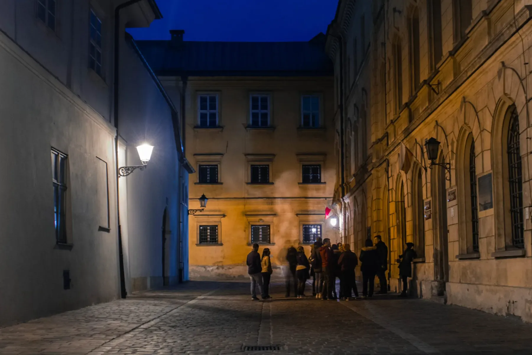 Eine Reisegruppe steht nachts auf einer engen, laternenbeleuchteten Kopfsteinpflasterstraße in Krakau.