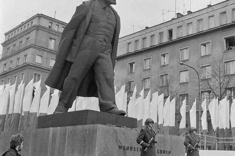 Schwarz-Weiß-Archivfoto der großen Lenin-Statue in Nowa Huta, mit zwei Soldaten, die an ihrem Sockel Wache stehen.
