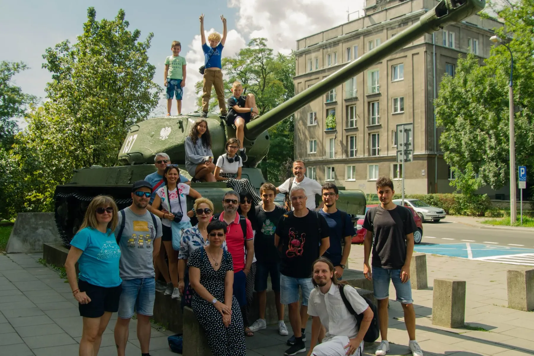 Reisegruppe aus Erwachsenen & Kindern posiert für ein Foto auf und um ein grünes IS-2-Panzerdenkmal in Nowa Huta, Krakau.