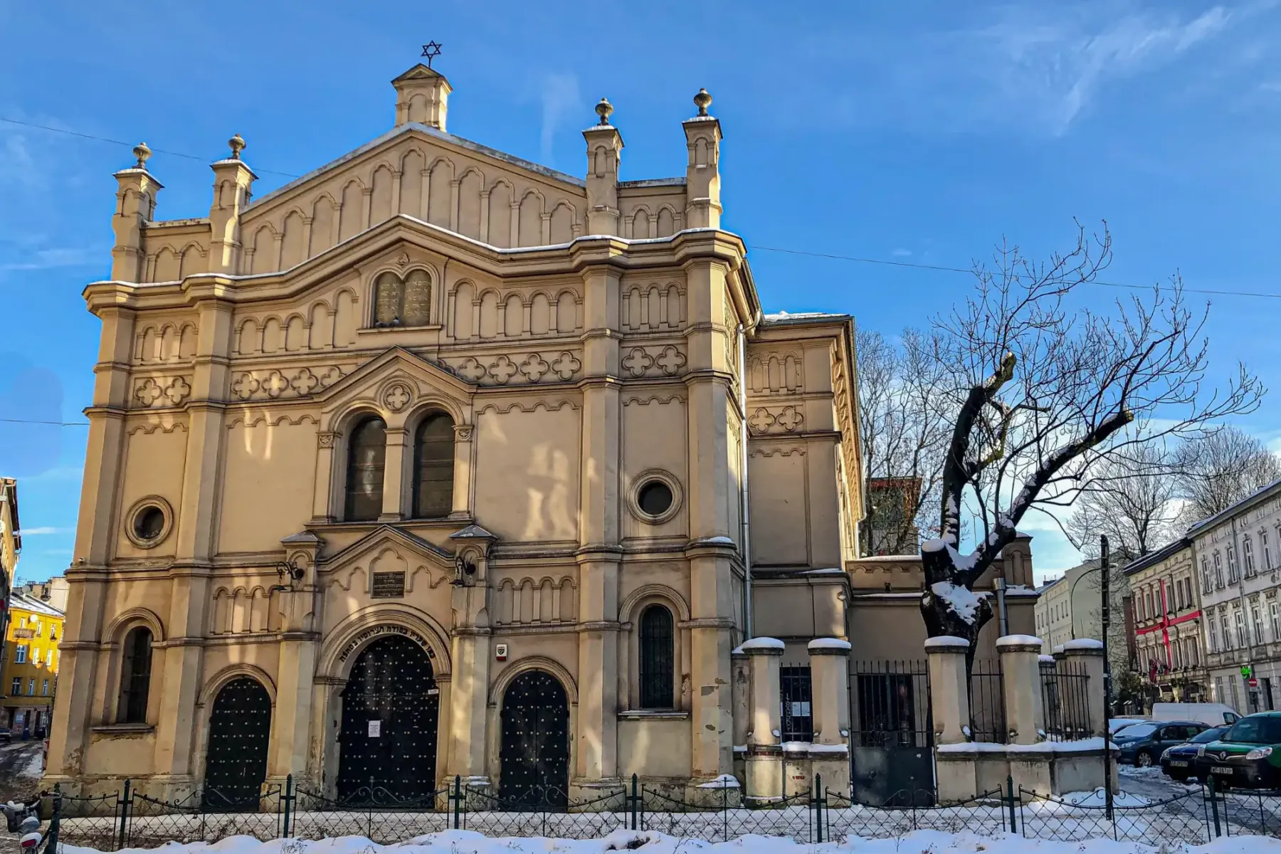 Vista exterior de una gran sinagoga ornamentada con la Estrella de David, cubierta de nieve, bajo un cielo azul en Cracovia.