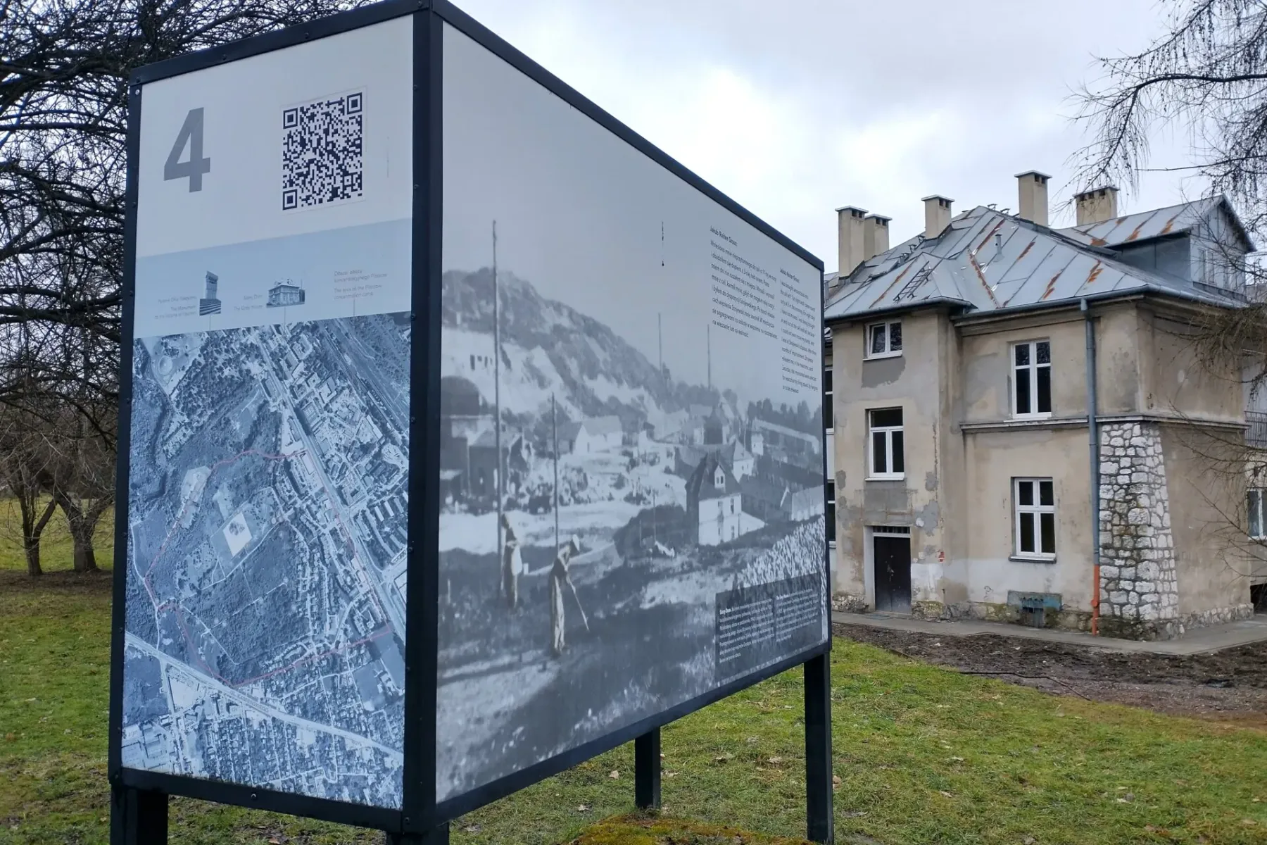 Eine Informationstafel mit Karte und historischen Fotos steht auf einer Wiese vor dem „Grauen Haus“ auf dem Lagergelände P...