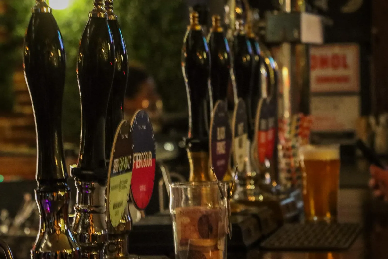 Eine Reihe glänzender schwarzer Zapfhähne auf einer Holztheke in einem schwach beleuchteten Krakauer Pub. Im Hintergrund e...