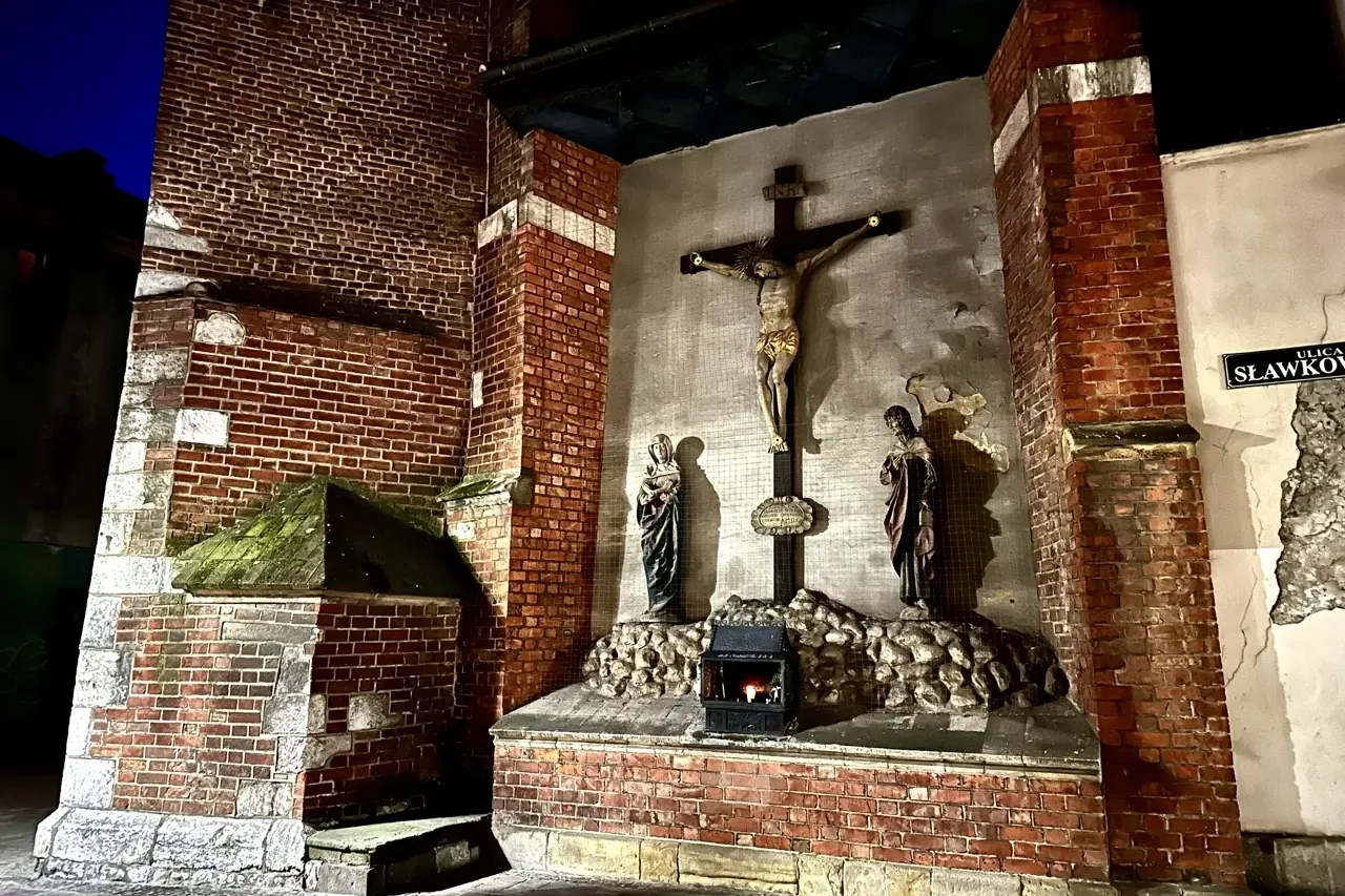 Ein Straßenschrein mit einem Kruzifix in einer Backsteinmauer in der Sławkowska-Straße in Krakau bei Nacht.