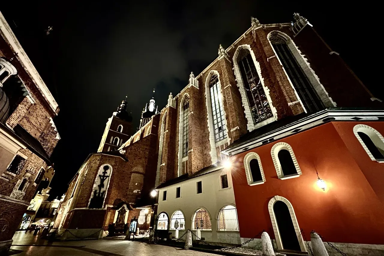 Marienbasilika in Krakau bei Nacht, zeigt Ziegelfassade, gotische Fenster und zwei Türme unter dunklem Himmel.