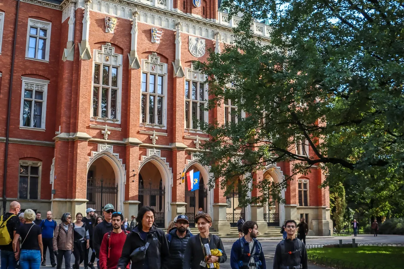 Eine Reisegruppe geht an einem sonnigen Tag an der neugotischen Backsteinfassade des Collegium Novum in Krakau vorbei.