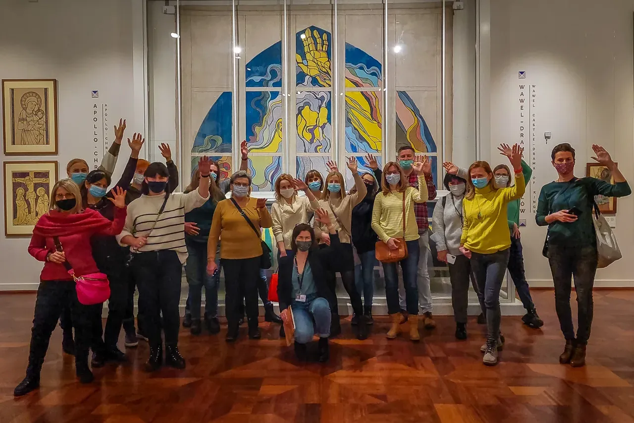 Eine Gruppe von Touristen mit Gesichtsmasken winkt in einem Museum vor einem großen, modernen Kunstwerk.