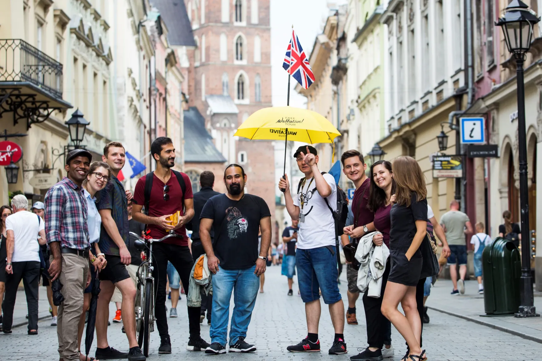 Eine Gruppe Touristen mit einem Reiseführer, der einen gelben Schirm auf einer Gasse in der Krakauer Altstadt hält.