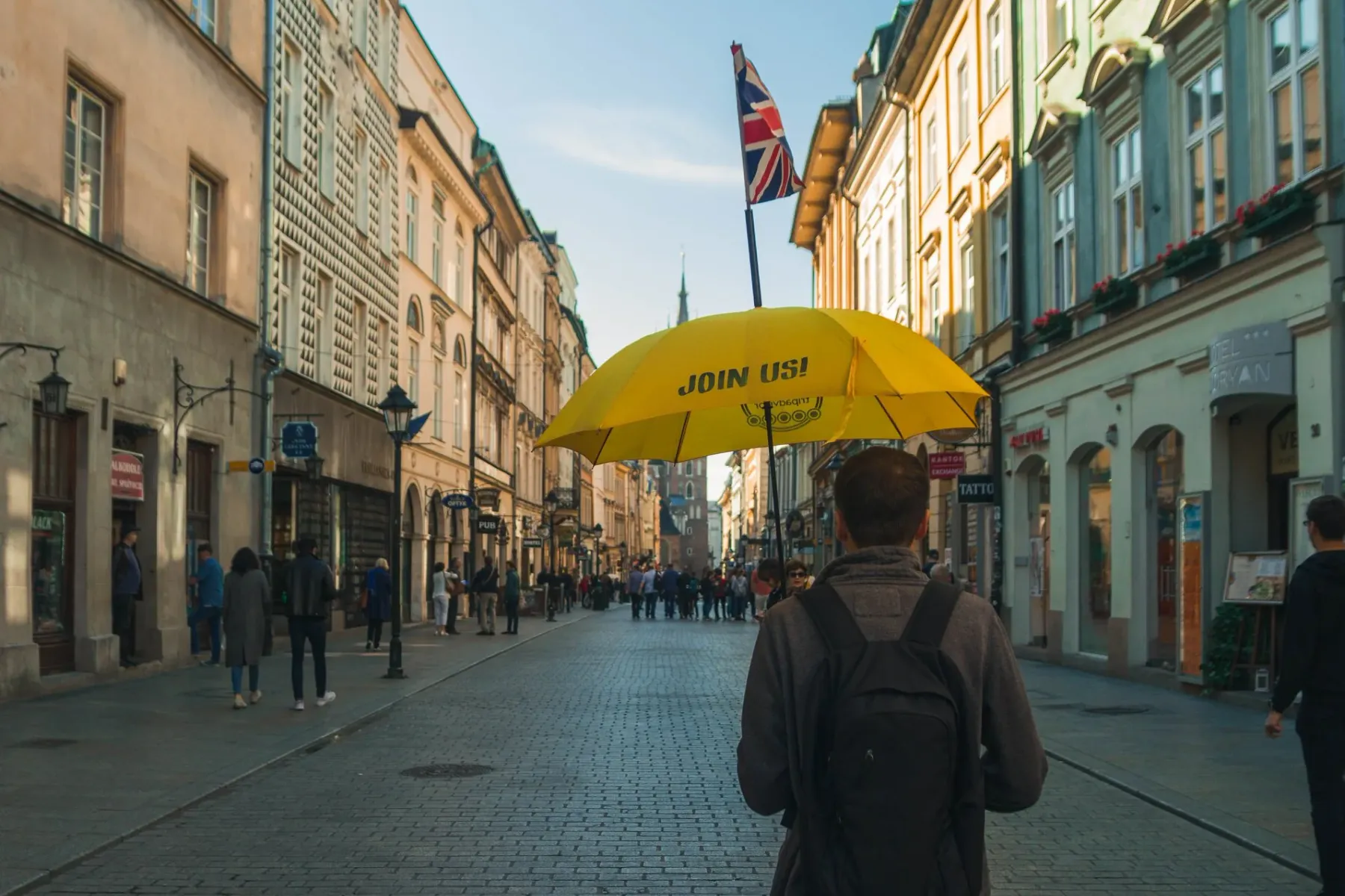 Ein Reiseführer hält einen gelben Schirm auf einer historischen Kopfsteinpflasterstraße in Krakau und führt eine Gruppe.