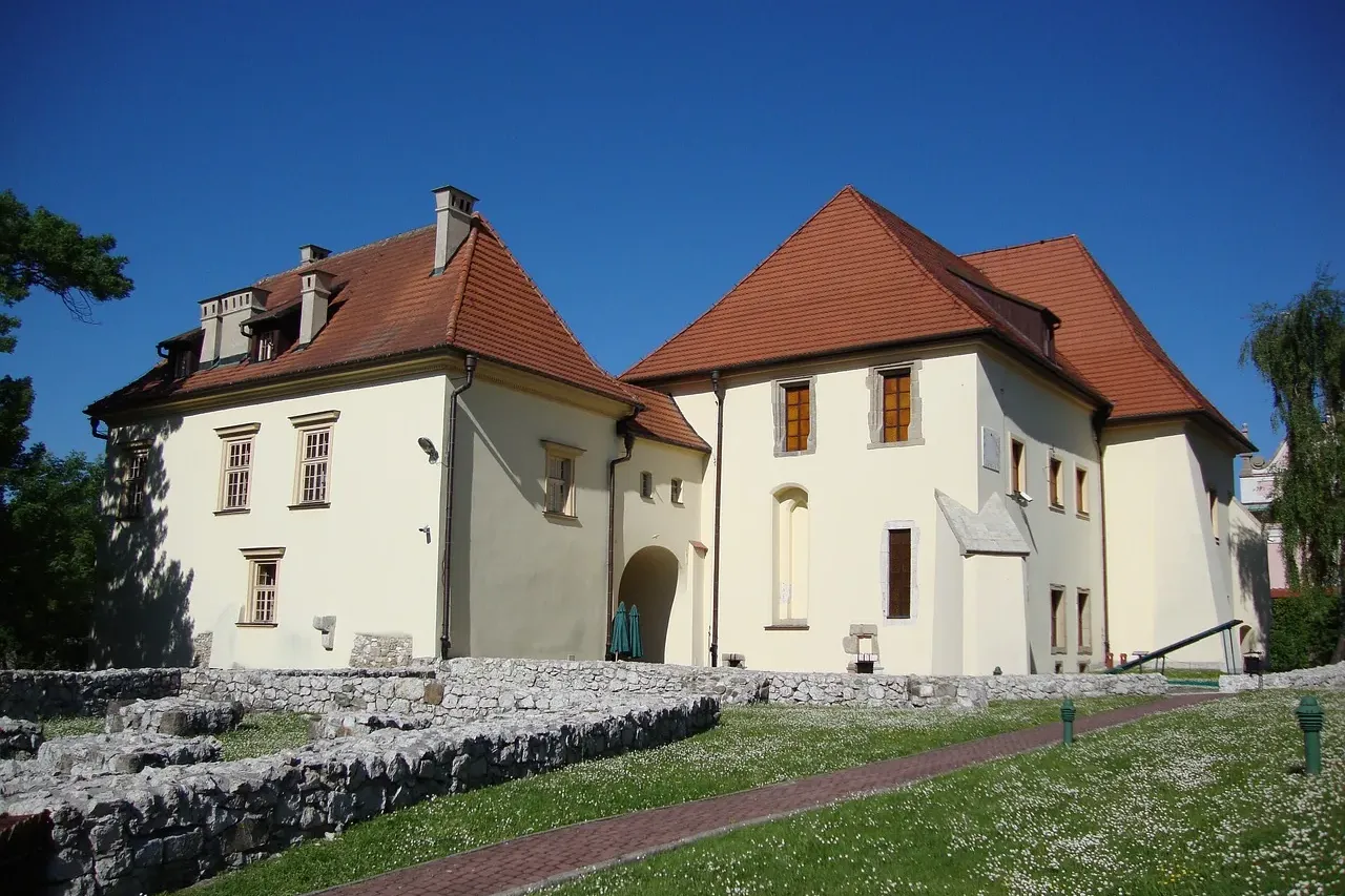 Historische weiße Gebäude mit roten Ziegeldächern am Salzbergwerk Wieliczka, mit alten Steinfundamenten auf einer Wiese.