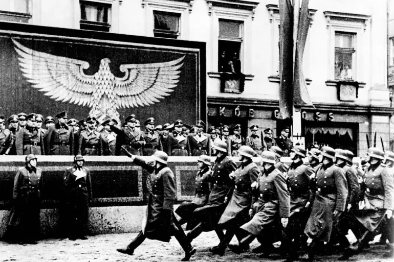 Schwarz-Weiß-Foto einer NS-Militärparade in Krakau. Soldaten marschieren an einer Tribüne mit Offizieren und einem großen ...