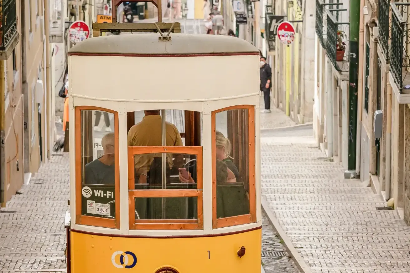 Gelbe Standseilbahn fährt eine steile gepflasterte Straße zwischen historischen Gebäuden in Lissabon hinauf.