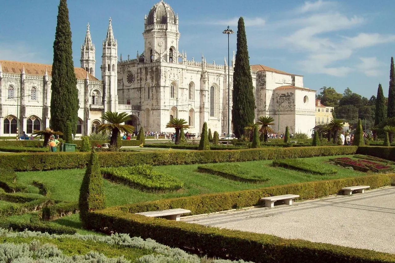 Das Hieronymuskloster in Lissabon mit gepflegten grünen Gärten im Vordergrund an einem sonnigen Tag.
