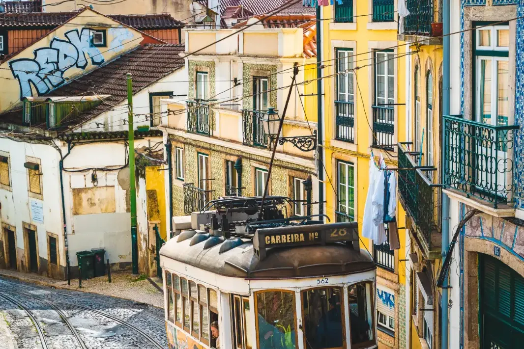 Die gelbe Straßenbahn 28 fährt eine steile Kopfsteinpflasterstraße mit traditionellen Gebäuden in Lissabon hinauf.
