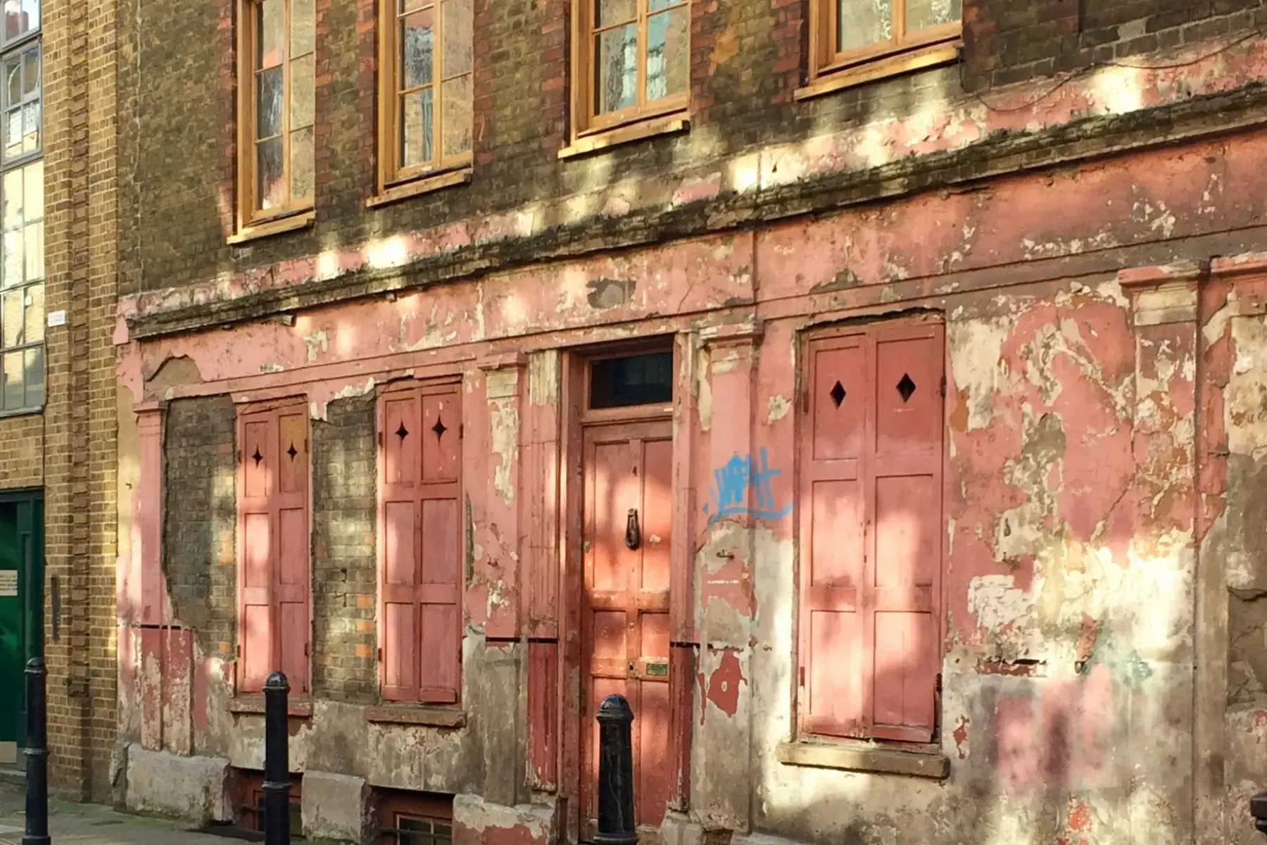A 1700s weathered brick building with a faded pink ground-floor storefront, viewed from a street in London.