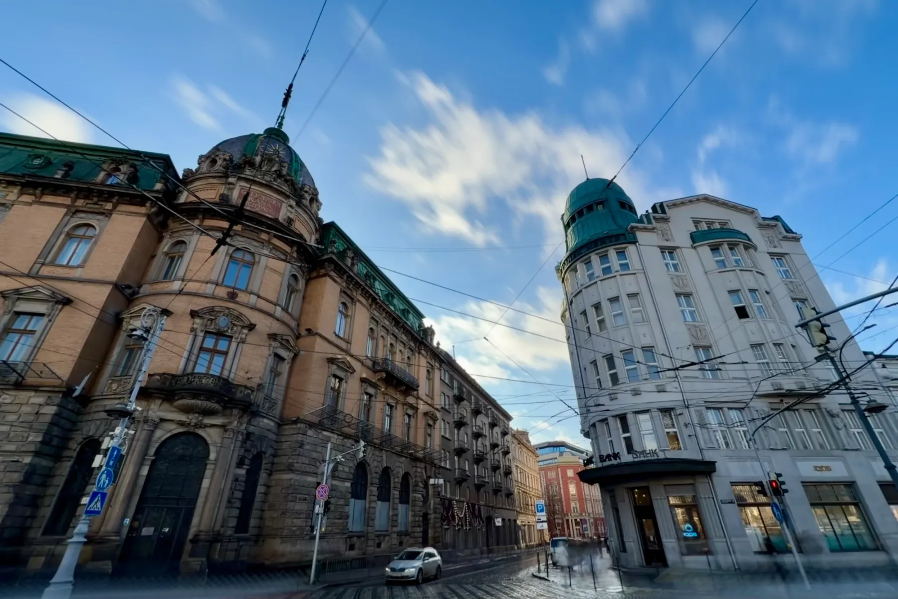 Weitwinkelaufnahme von zwei historischen Gebäuden an einer nassen Kopfsteinpflasterstraße in Lemberg unter blauem Himmel.