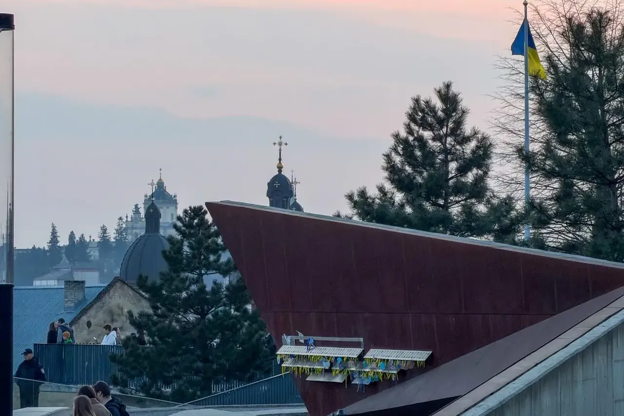 Lemberger Skyline mit Kirchendomen, einem modernen Gebäude, Menschen auf einem Weg und einer ukrainischen Flagge bei Dämme...