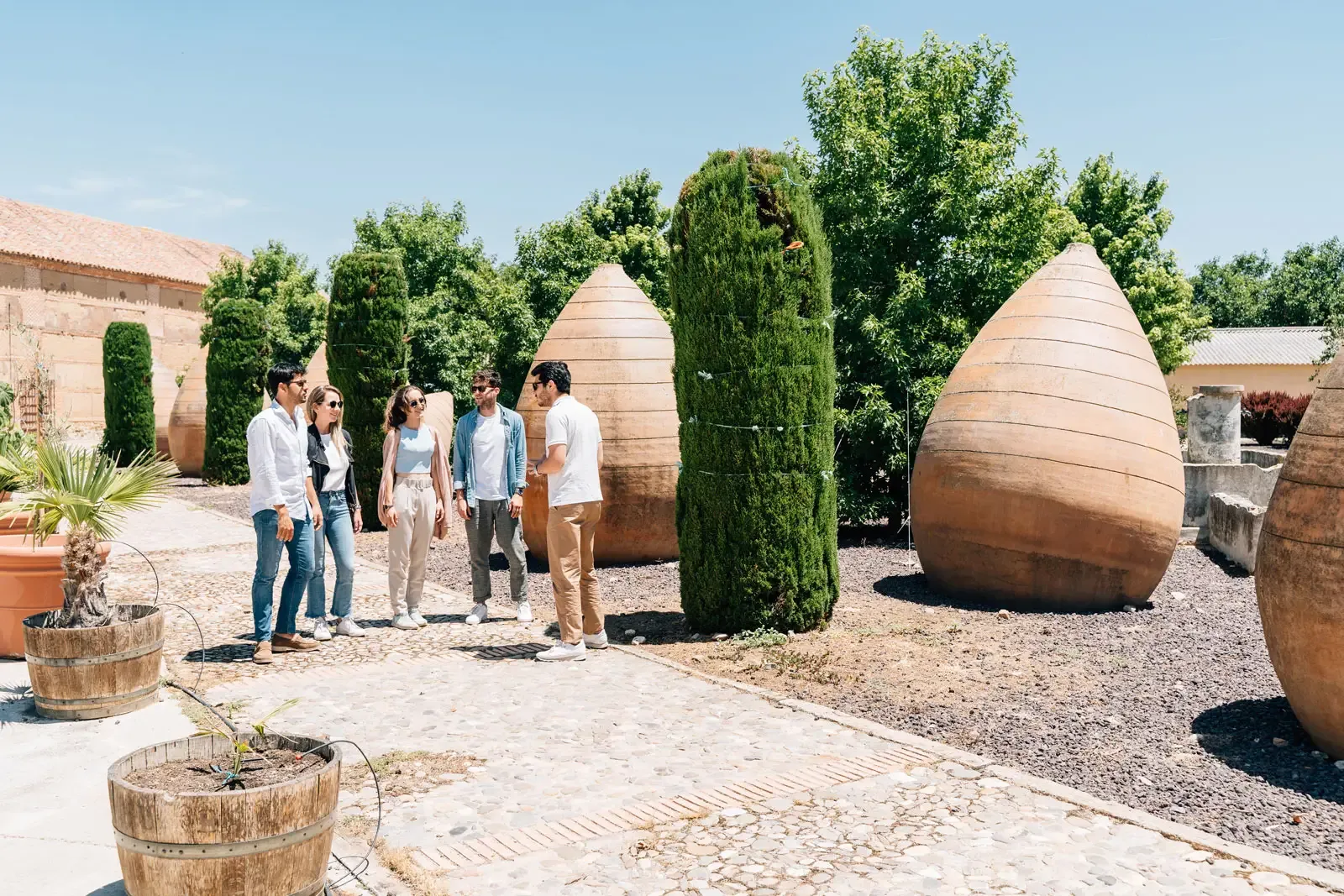 Un guía turístico habla con un pequeño grupo de personas en un patio soleado con grandes tinajas de barro de estilo antiguo.