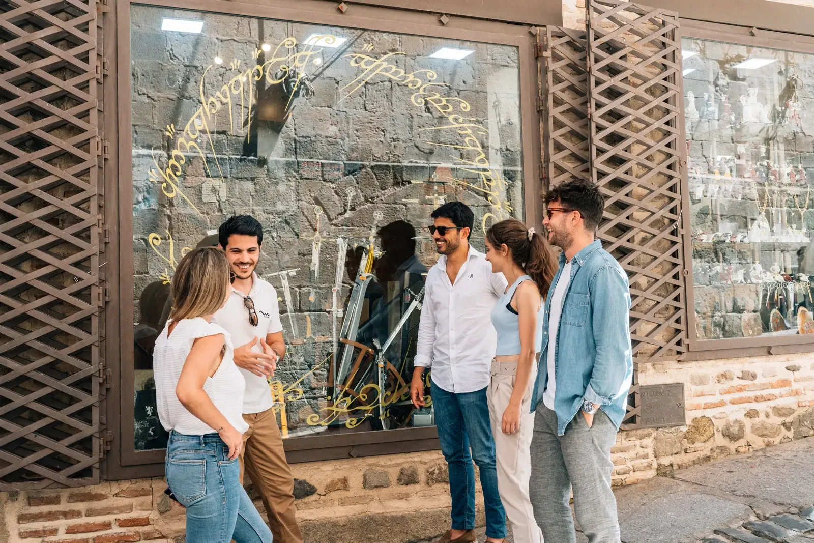 Eine Gruppe von fünf jungen Erwachsenen unterhält sich vor einem Geschäft mit goldener Schrift auf dem Schaufenster.