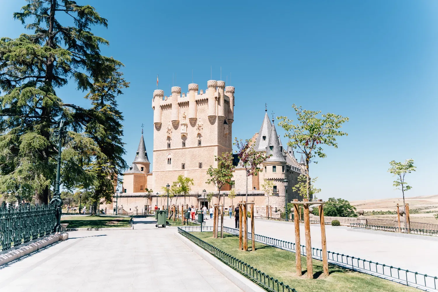 Der Alcázar von Segovia, eine Steinburg mit Türmen, von einem Park an einem sonnigen Tag aus gesehen.