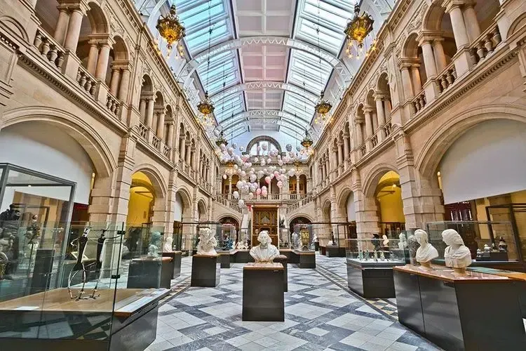 Interior of the Kelvingrove Art Gallery and Museum in Glasgow, with stone pillars, a glass roof, and sculpture exhibits.
