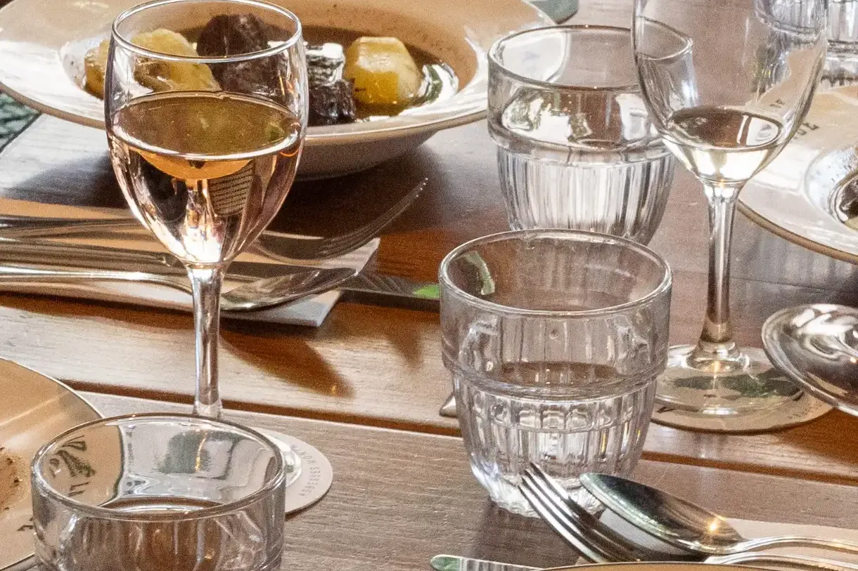 Ein gedeckter Restauranttisch mit Eintellergerichten, auf einem 'ADÉLAÏDE', Wasser- und Roséweingläsern sowie einem Brotkorb.