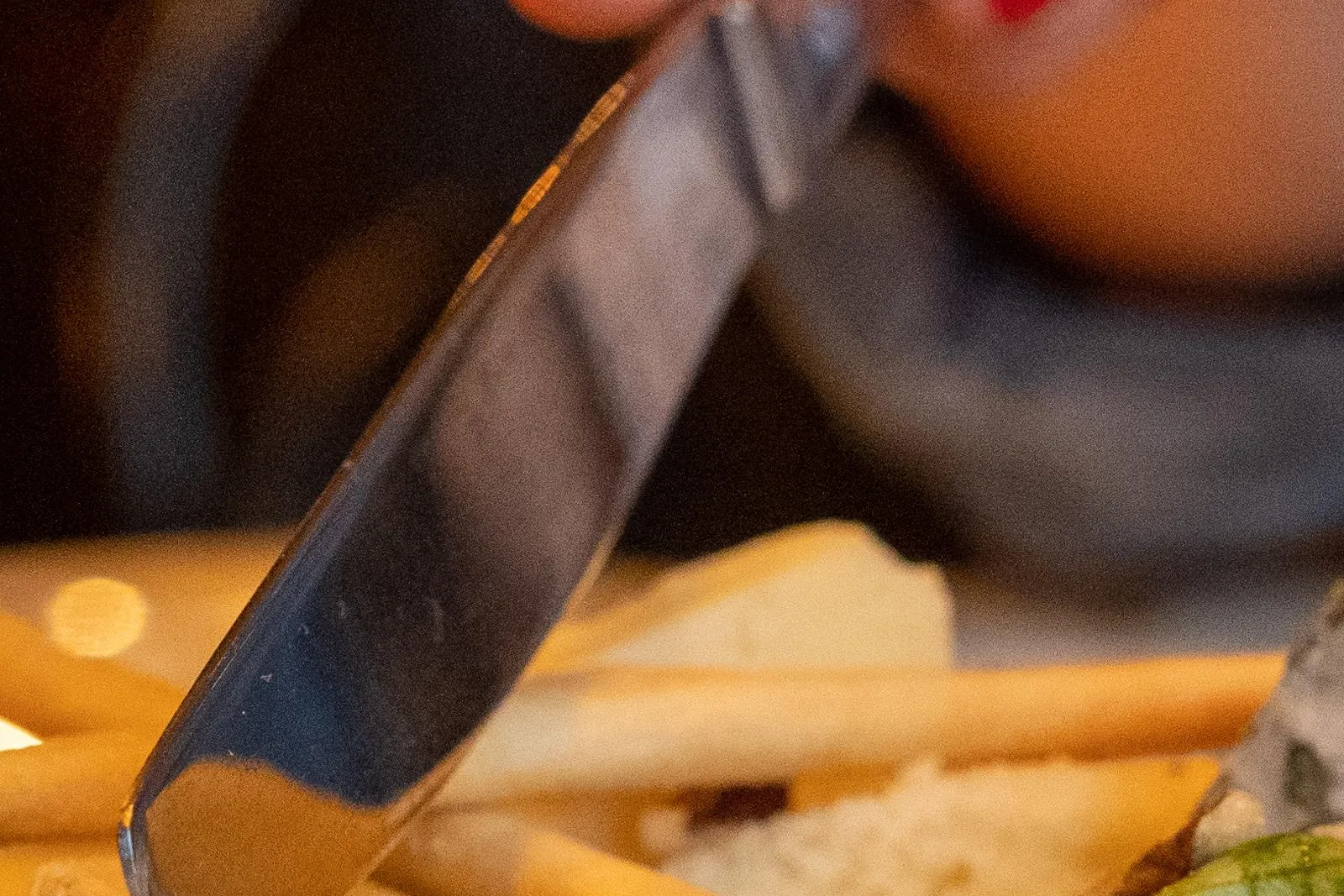 Primer plano de una mano con esmalte rojo cortando un trozo de queso de corteza blanca en un plato con palitos de pan.