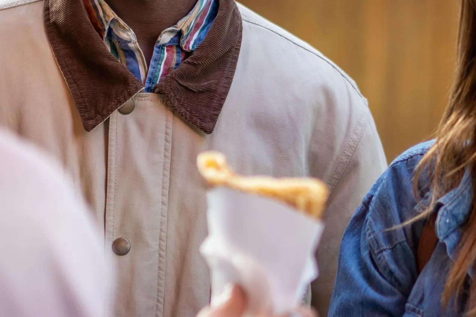 Hombre sonriente observando cómo se entrega un crêpe a una persona con chaqueta vaquera en la calle.
