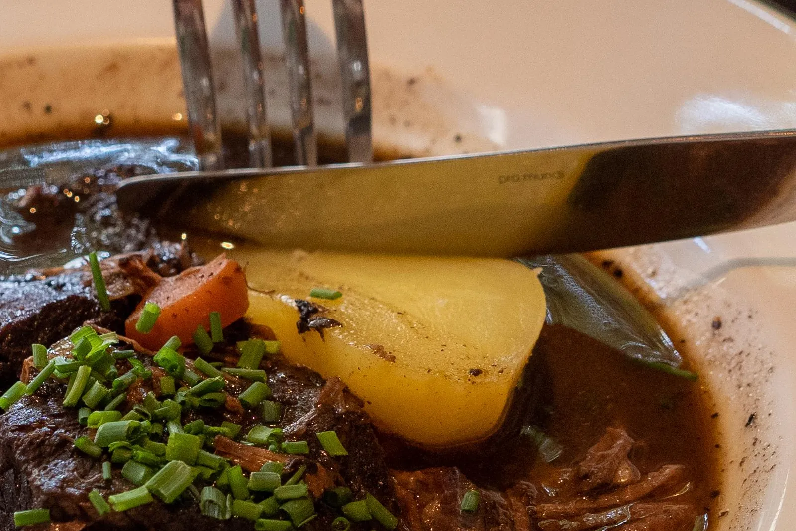 Primer plano de un estofado francés con patata y cebollino fresco, un tenedor y cuchillo cortando la comida.