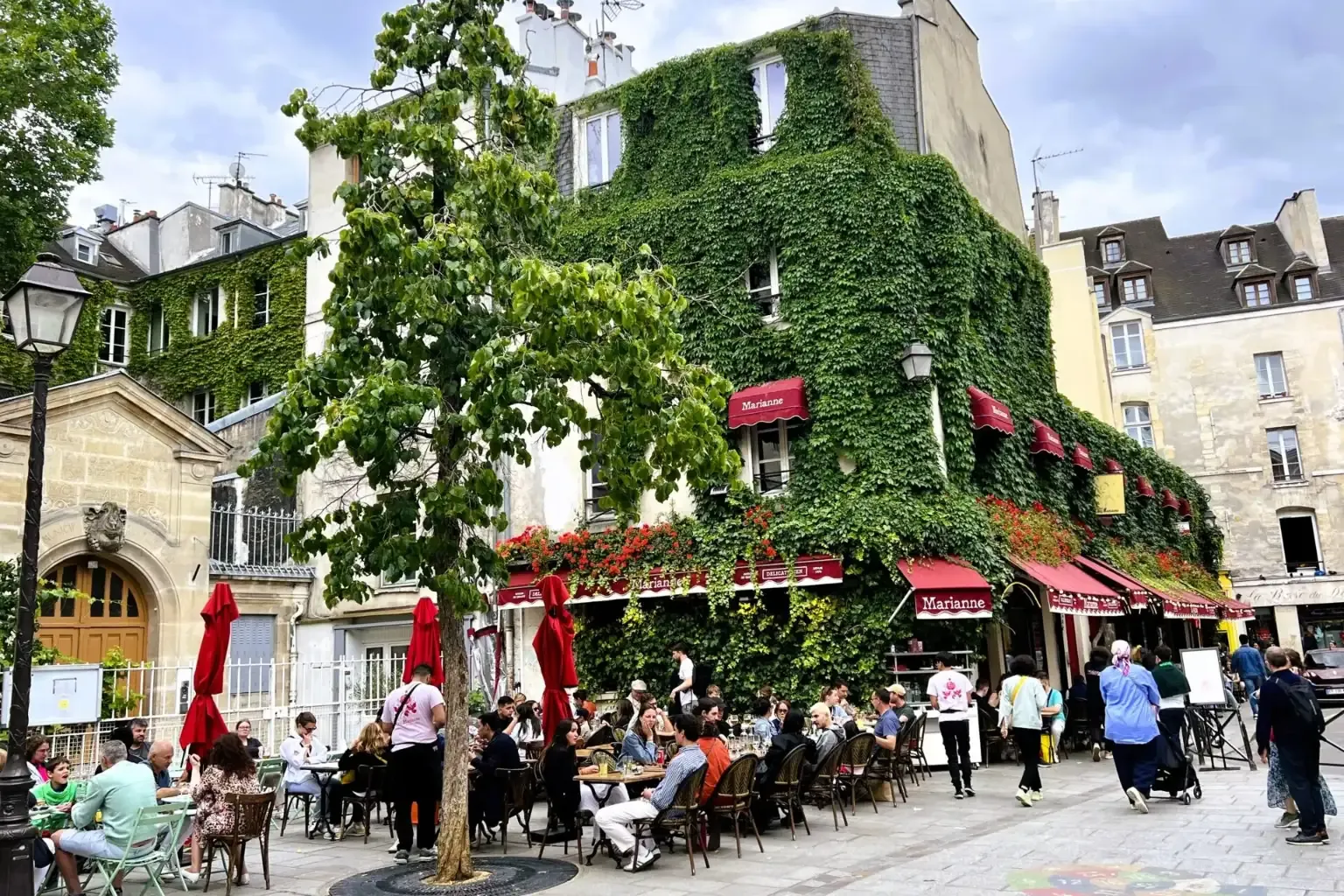 Ein mit grünem Efeu und roten Markisen bedecktes Gebäude in Paris, mit einer Außenterrasse des Restaurants und Gästen.
