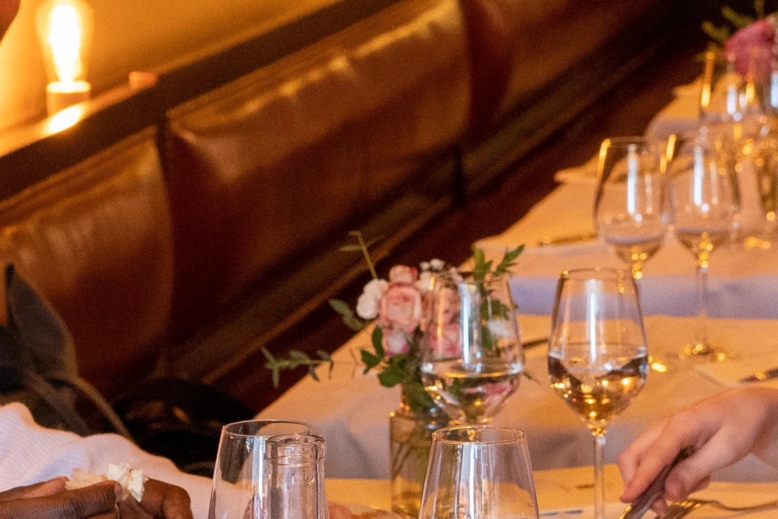 Personas cenando en una mesa de restaurante con pan, botella de agua, copas de vino y una tabla de quesos.