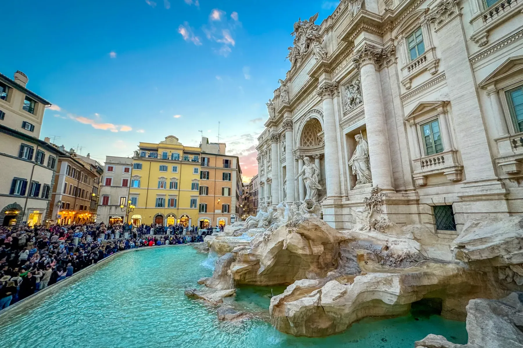 Abarrotada Fontana di Trevi en Roma al atardecer, con esculturas barrocas, agua turquesa y edificios históricos bajo un ci...