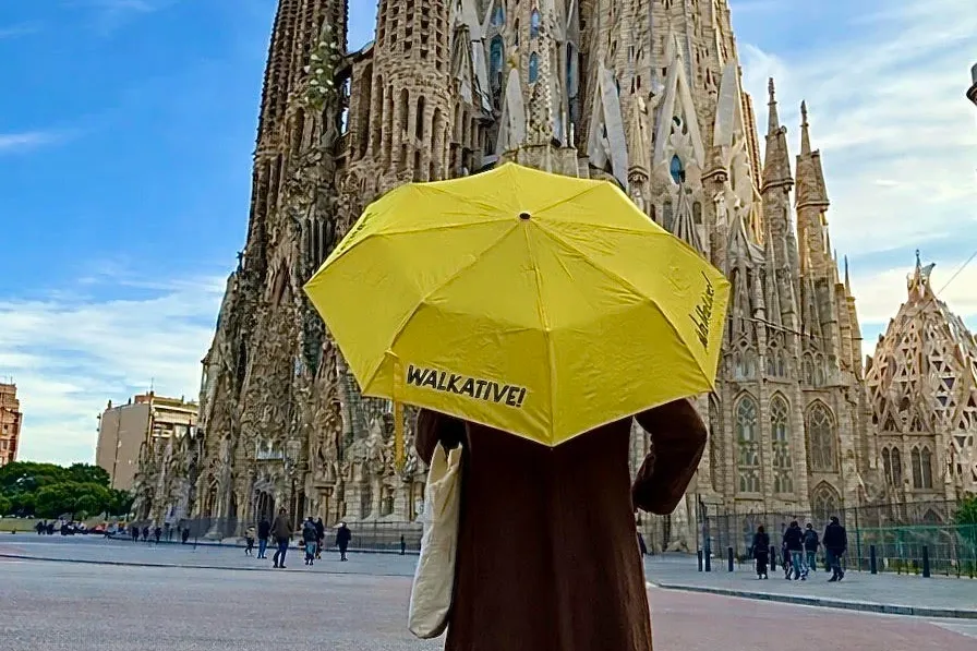 Person mit gelbem Walkative-Regenschirm, dem komplizierten Turm der Sagrada Família unter blauem Himmel in Barcelona zugew...