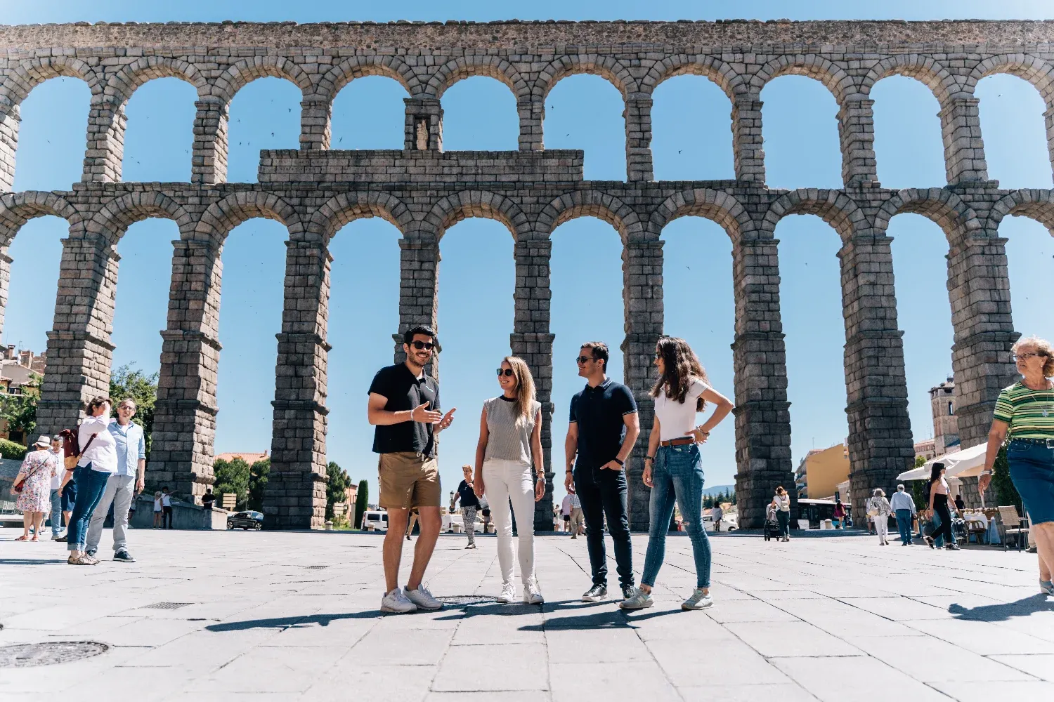 Ein Reiseführer spricht mit drei Touristen vor dem großen, sonnigen Aquädukt von Segovia in Spanien.