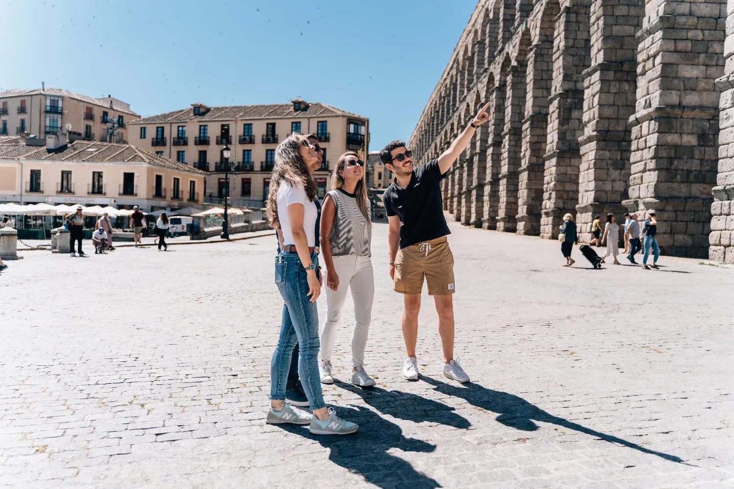 Ein Reiseführer zeigt drei Touristen an einem sonnigen Tag das Aquädukt von Segovia.