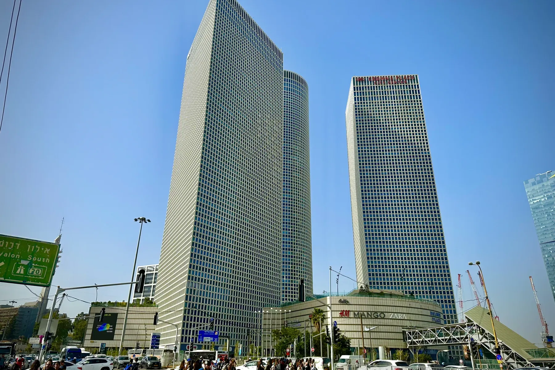 Modern skyscrapers of Azrieli Center dominate the skyline in Tel Aviv, with a busy street, pedestrians, and cars below on ...