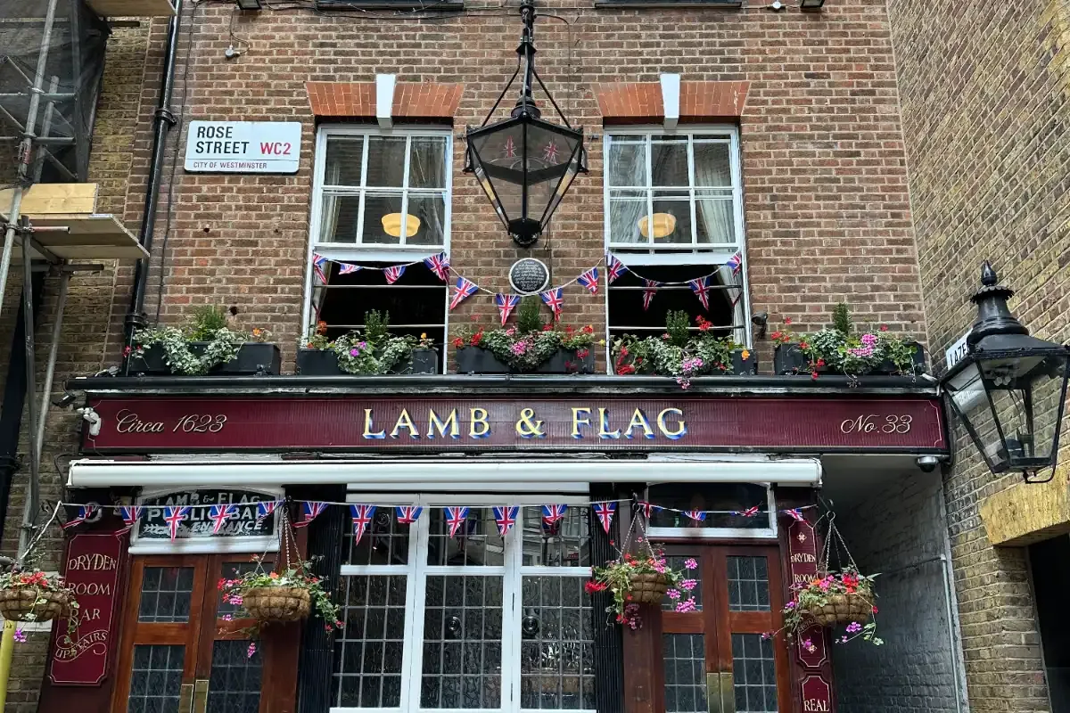 La fachada de ladrillo del histórico pub Lamb & Flag en un estrecho callejón de Londres, decorada con flores y banderas br...