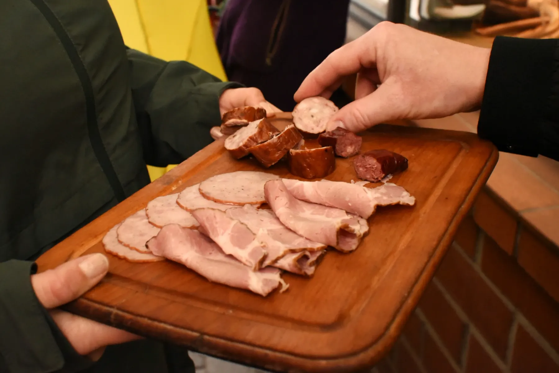 Two people sharing a wooden board with traditional sliced meats and sausage tasting portions.
