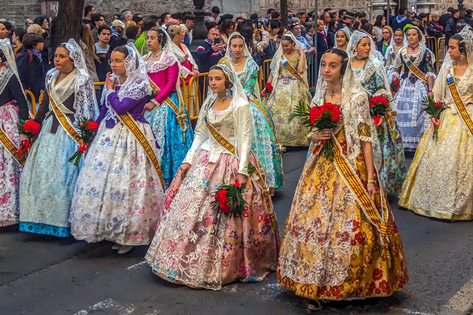 Un grupo de mujeres y niñas con coloridos y tradicionales trajes de fallera durante un desfile en Valencia.