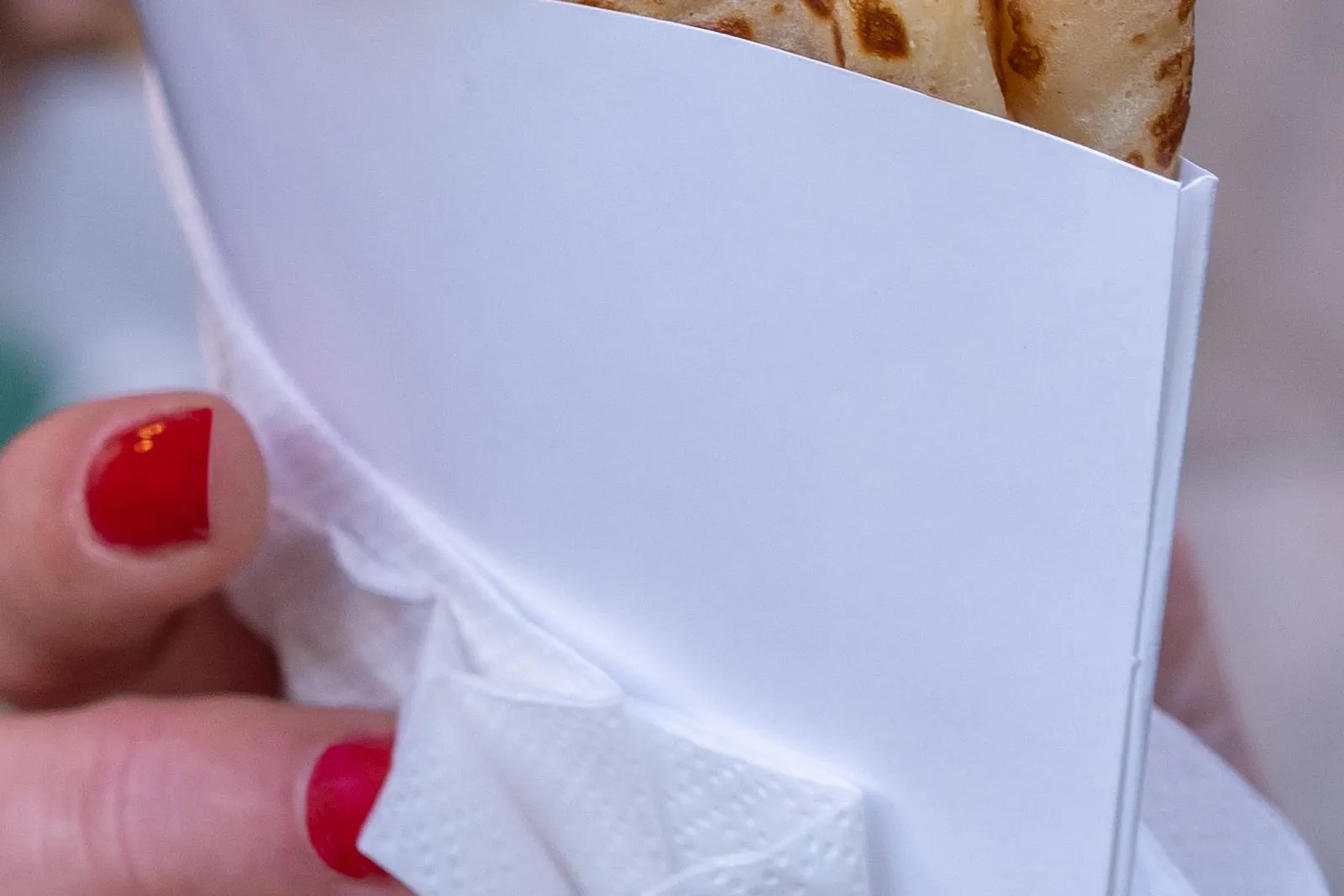 Primer plano de una mano con esmalte de uñas rojo sosteniendo un crepe doblado en un soporte de papel blanco.