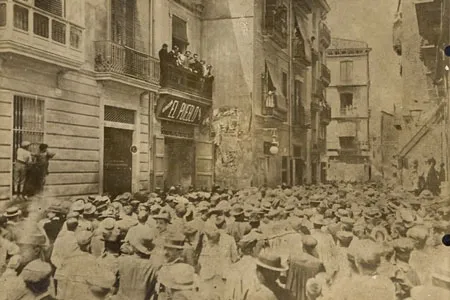 Historic, sepia-toned photo of a crowd gathered on a street in Valencia, in front of the 'El Pueblo' newspaper building.