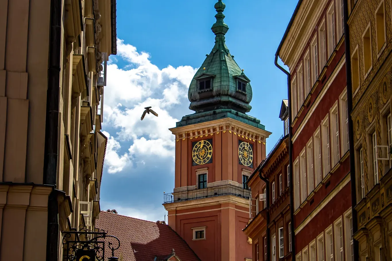 Vista de una calle estrecha hacia la torre del reloj del Castillo Real de Varsovia con cúpula verde, esferas doradas y un ...