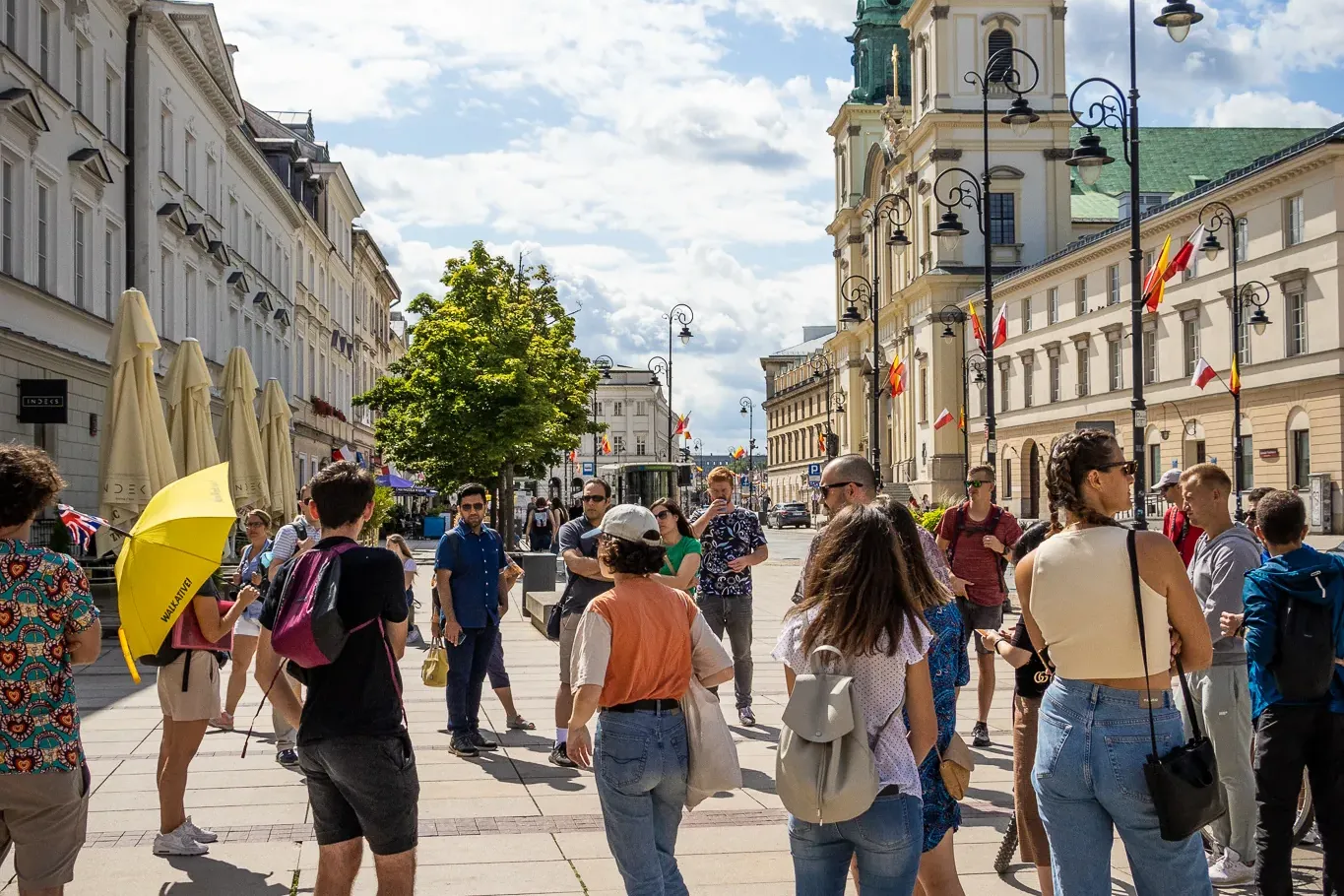 Un grupo de personas reunidas en una calle adoquinada de Varsovia con una iglesia histórica y edificios de fondo bajo un c...