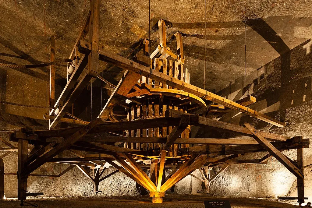Ein großes, historisches hölzernes Pferde-Göpelwerk im Salzbergwerk Wieliczka, mit Salzgesteinwänden im Hintergrund.