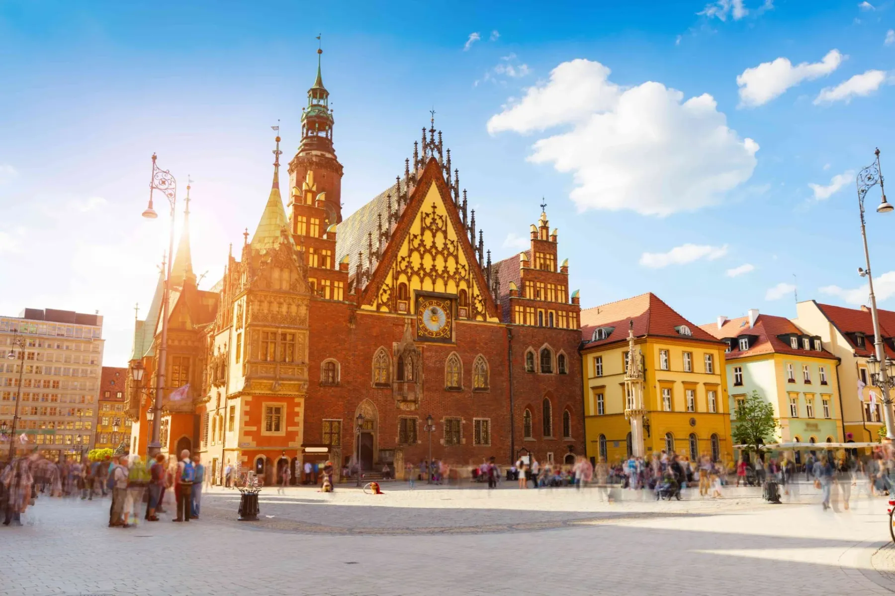 Wroclaw Old Town Hall and colorful surrounding buildings on Market Square, with blurred tourists and bright sunlight.