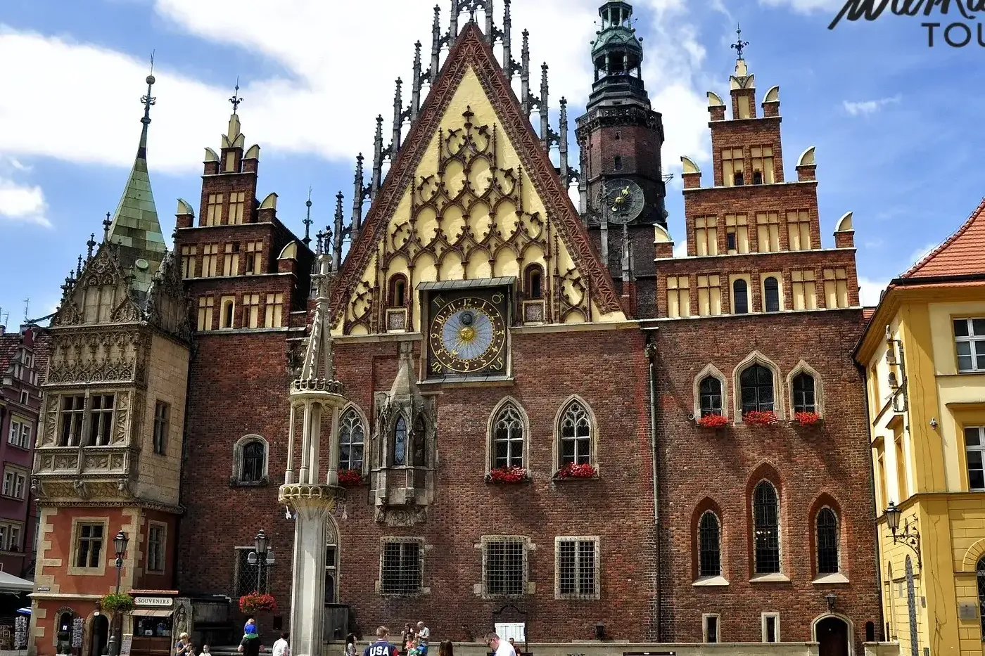Gothic brick Old Town Hall in Wroclaw with a large clock, ornate gables, and a tall spire. People are gathered in the cobb...