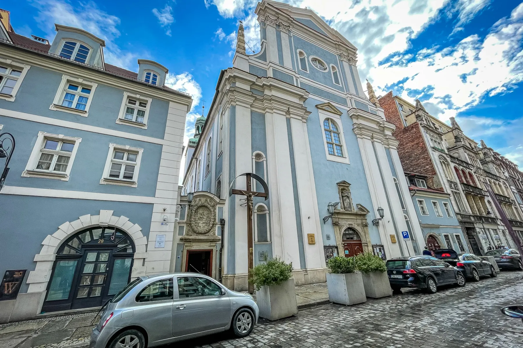 Jasnoniebieska barokowa fasada kościoła św. Antoniego z Padwy przy brukowanej ulicy we Wrocławiu pod błękitnym niebem.