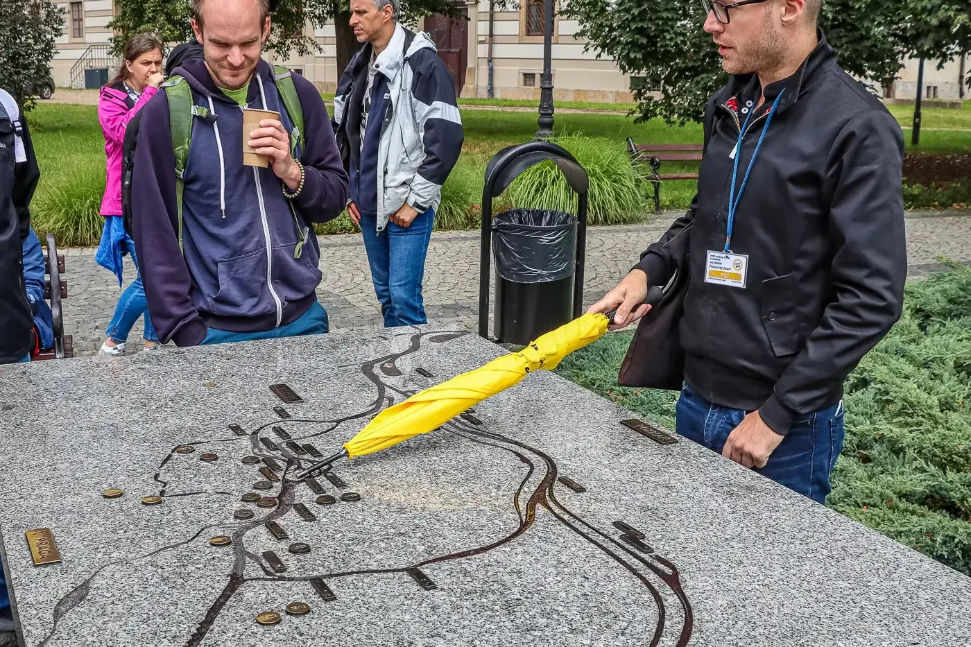 Przewodnik z żółtym parasolem wskazuje na dotykową mapę Wrocławia, a grupa turystów słucha.