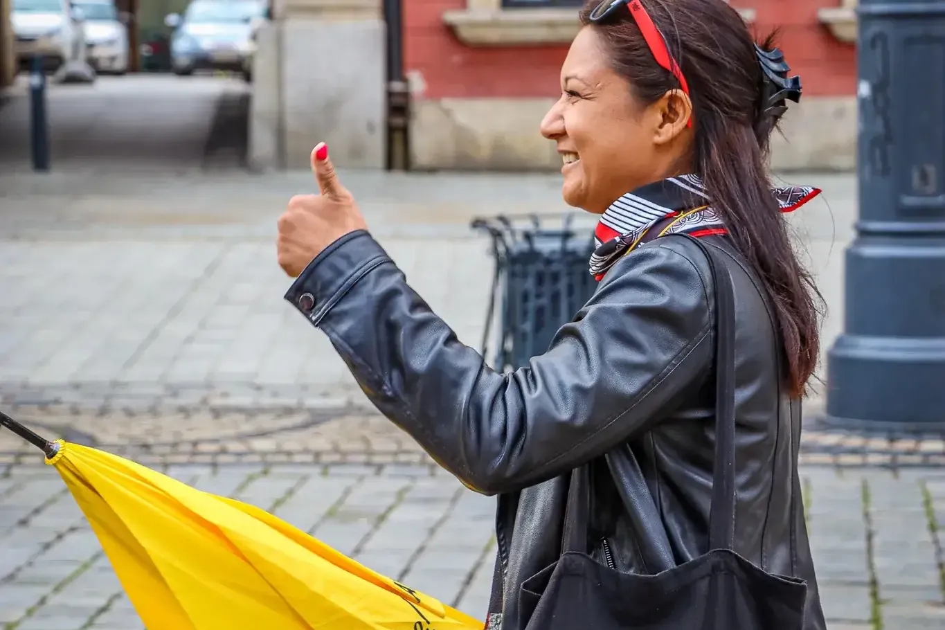 A female tour guide with a yellow Walkative umbrella gives a thumbs-up on a cobblestone street in Wroclaw.