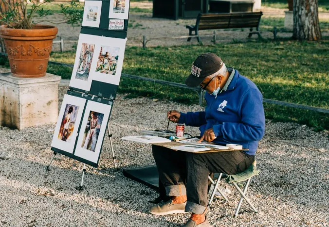 Street artist painting in a Roman park, showcasing artwork depicting famous landmarks.